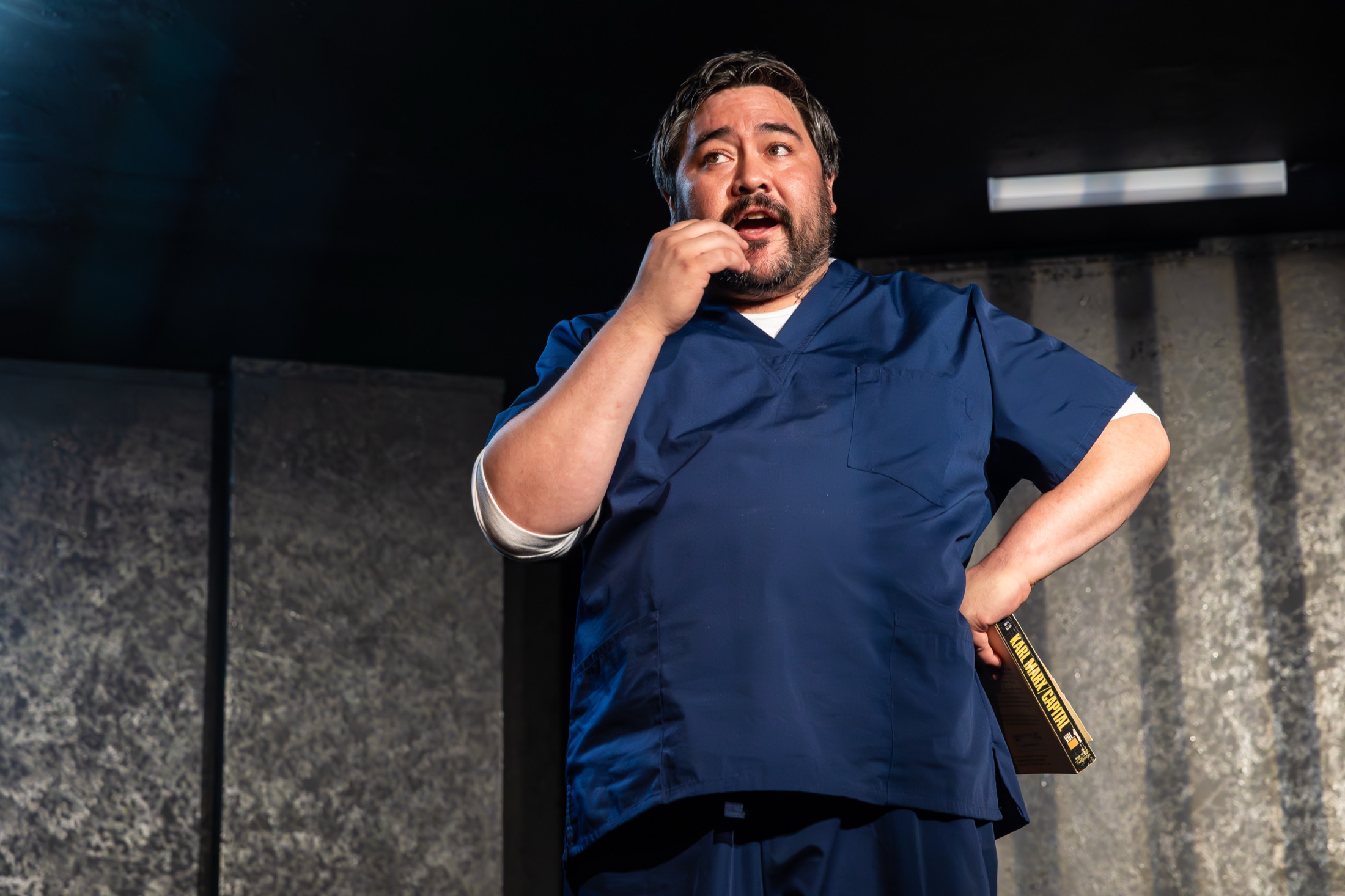 A performer speaks onstage against a stark prison-inspired set